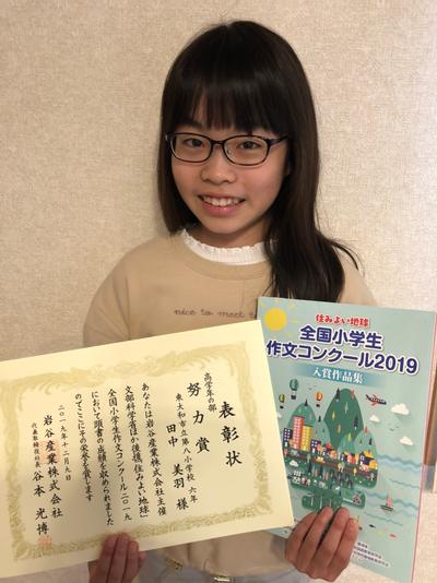 写真：表彰状と作文が掲載された冊子を持つ田中さん