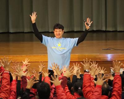 子どもたちと手を挙げて運動する岩隈選手の写真